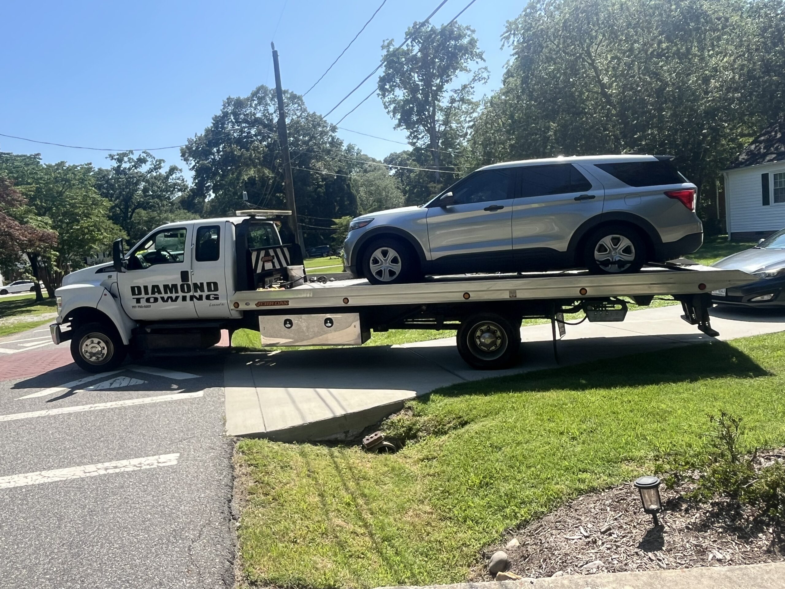 Diamond Towing flatbed carrying a silver SUV in a residential neighborhood